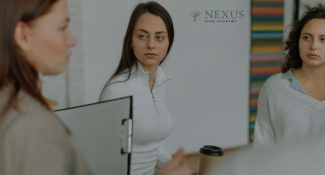 Teen girl in a group setting, holding a coffee cup, listening attentively to a peer, symbolizing 'Top Arizona-Based Activities for Teens with ADHD' to foster engagement and interaction.
