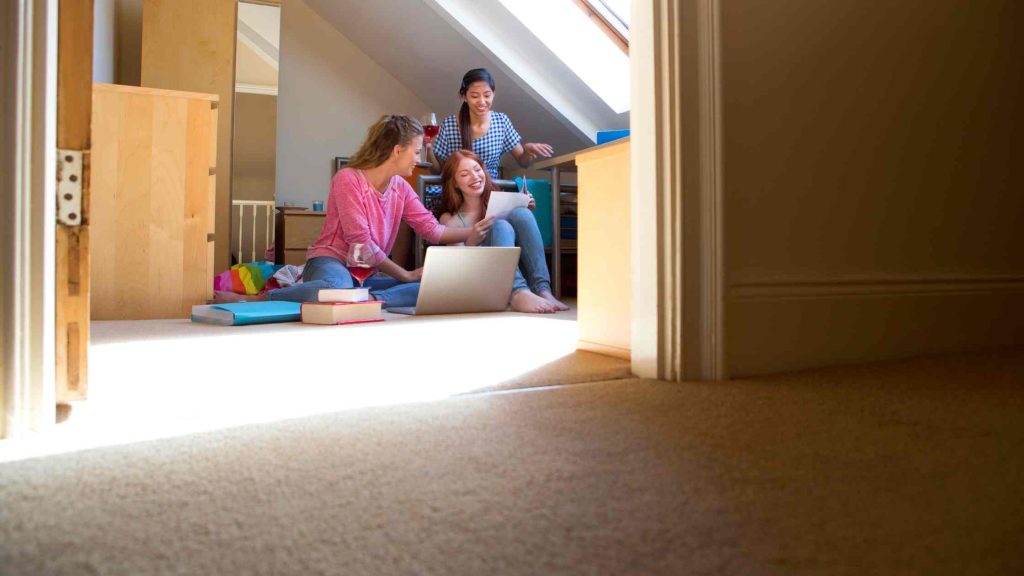 Three young women study together in a cozy attic room, using a laptop and books, symbolizing the importance of educational support and accommodations for learning success.
