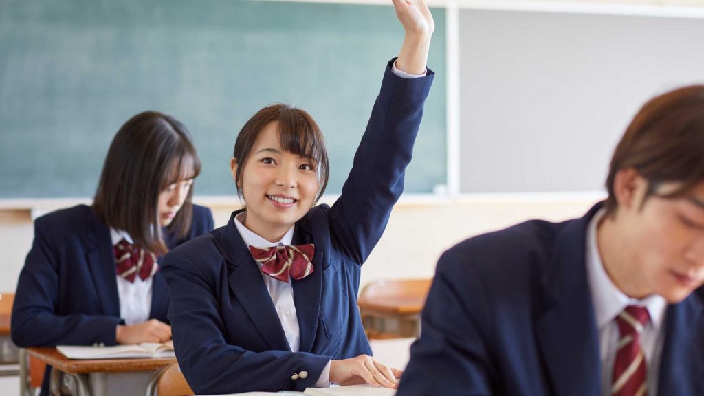 Student in uniform confidently raises hand in class, demonstrating engagement and participation—key principles in applying effective communication techniques