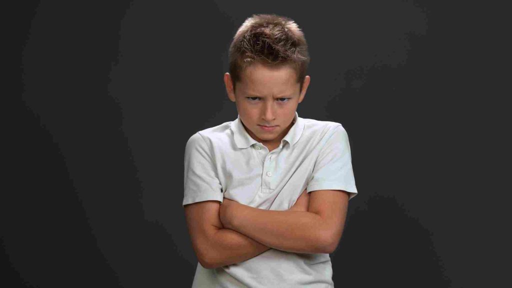 A frustrated teen boy crossing his arms, representing the need for structured anger management resources available for teen boys in Arizona to develop emotional regulation skills.