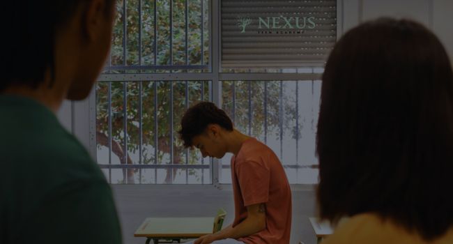 Image of a teen sitting at a desk at Nexus Teen Academy, reflecting on support strategies. This scene highlights the importance of understanding and coping with Disruptive Mood Dysregulation Disorder (DMDD).