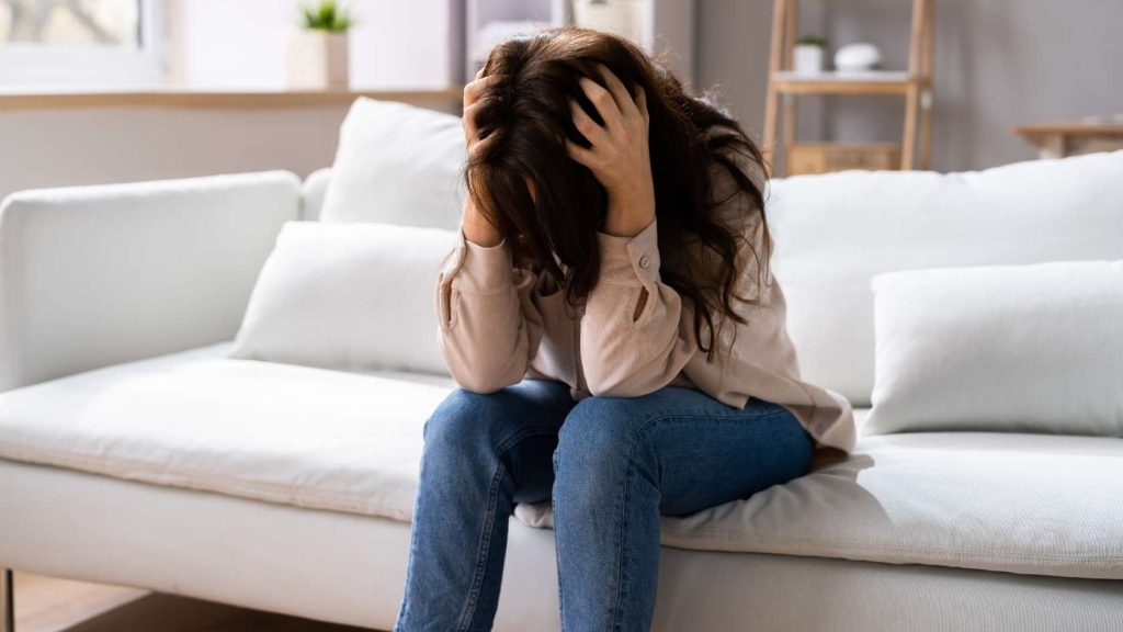 A distressed teen girl sits on a couch, holding her head in frustration, symbolizing emotional instability, anxiety, and distress—common symptoms of borderline personality disorder.
