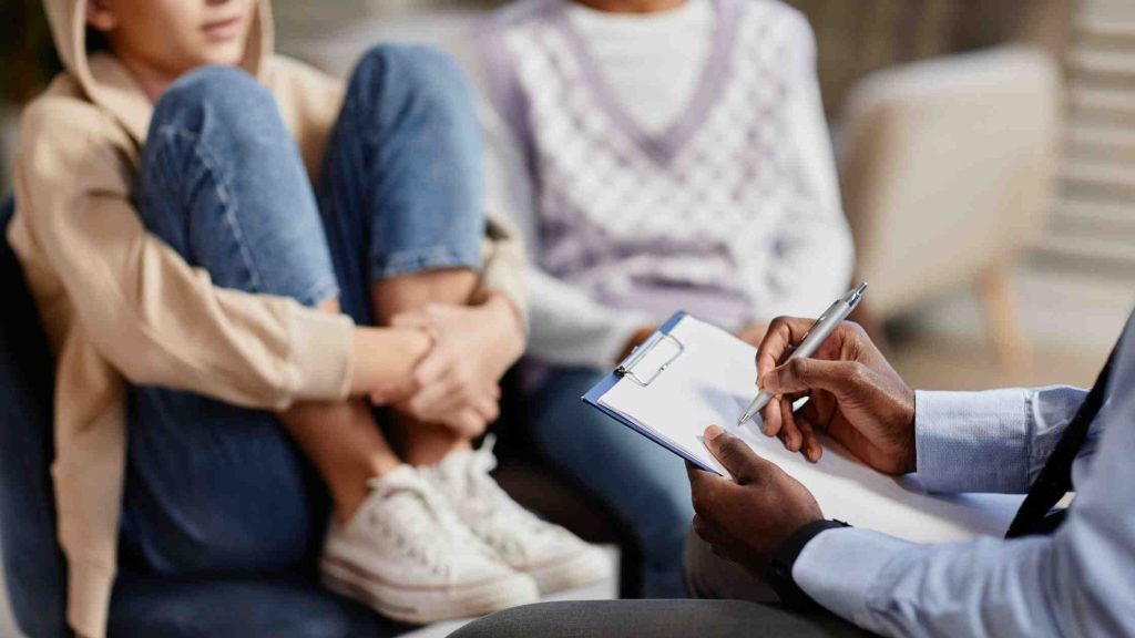 Therapist taking notes while engaging with a teen in a counseling session, illustrating interpersonal therapy techniques used to support adolescent mental health.