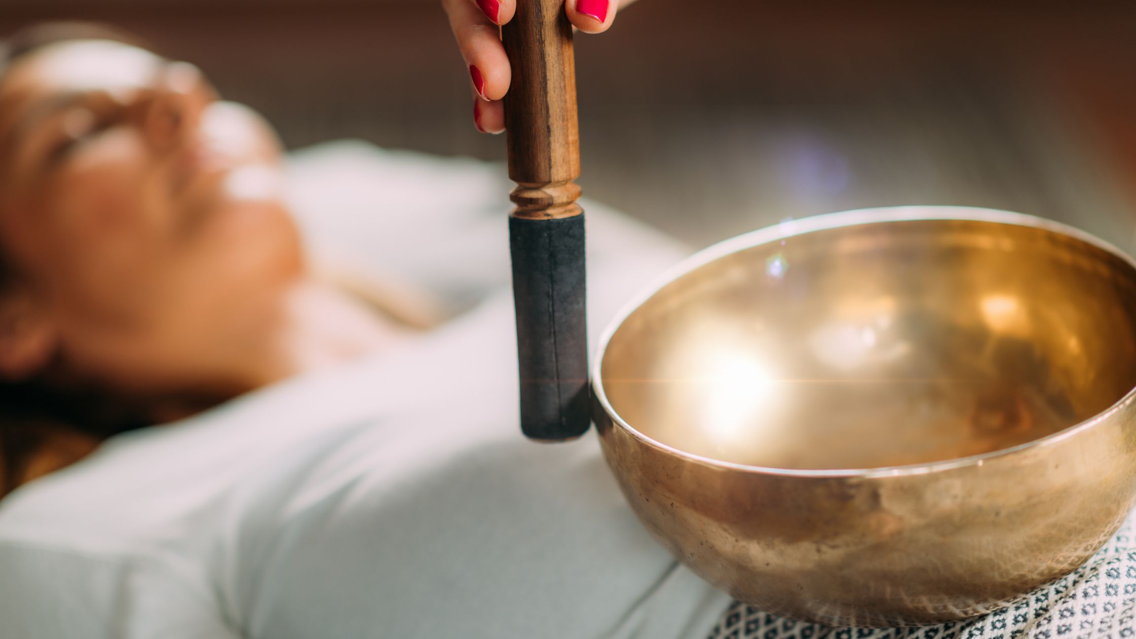 A person lying down receiving a sound healing session with a singing bowl, a practice that benefits individuals seeking relaxation, stress relief, and balance.
