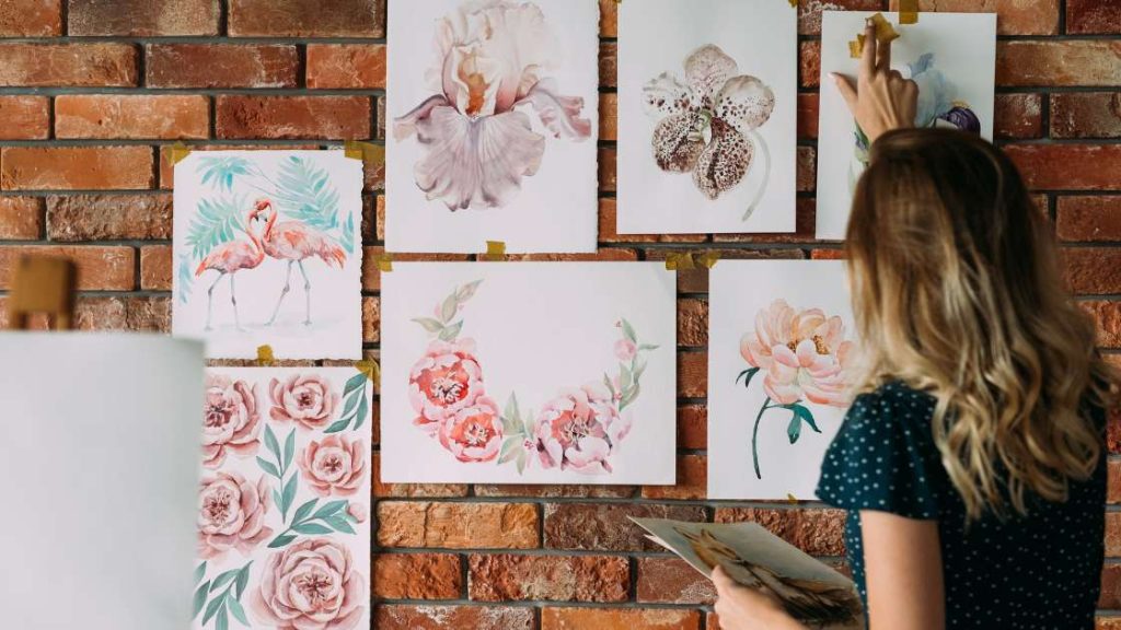 Teen girl arranging floral watercolor paintings on a brick wall, illustrating how art therapy fosters emotional expression, creativity, and self-esteem in adolescents.