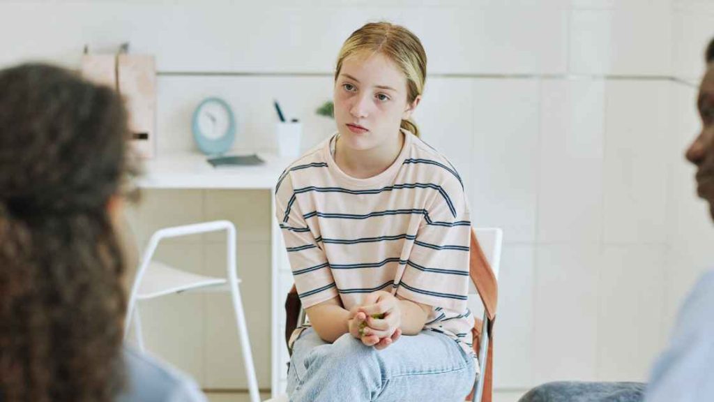 A teenage girl appears withdrawn during a group therapy session, symbolizing the emotional vulnerability and individual factors like trauma that influence the effectiveness of exposure therapy.