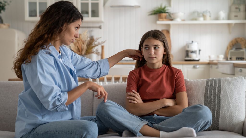 A concerned mother comforting her teenage daughter, who sits with crossed arms, representing ways to help teens with social anxiety.