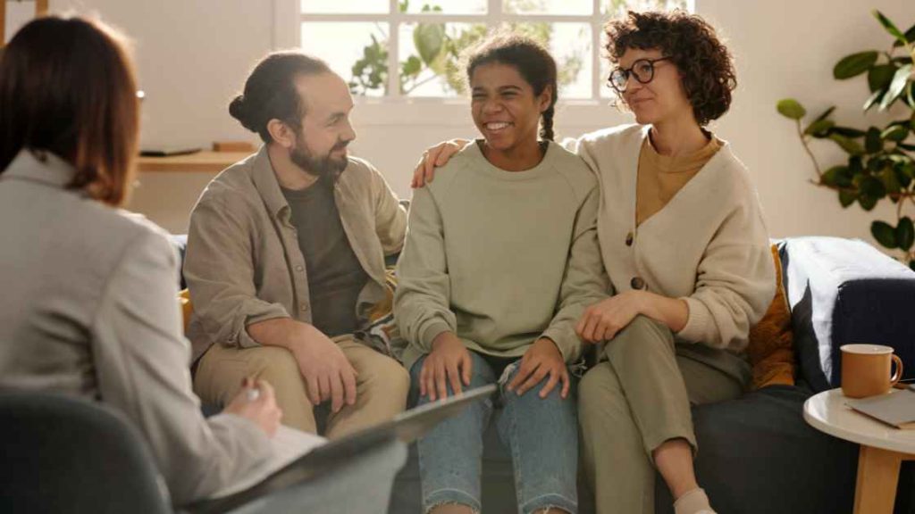 A smiling teen sits between two supportive parents during a therapy session, symbolizing the critical role of parental support in maximizing the effectiveness of exposure therapy.