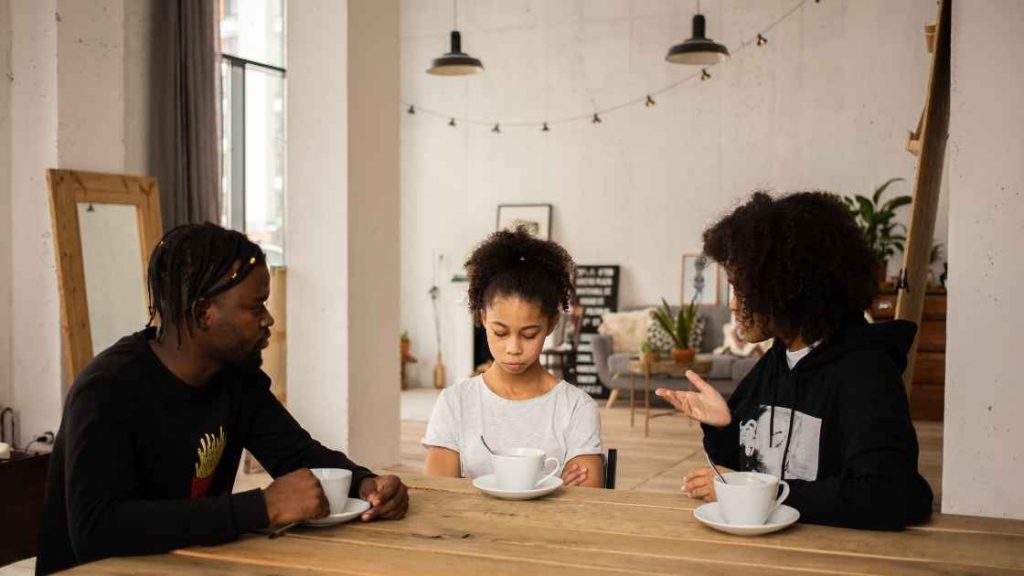 Parents sit at a table with their child in a calm setting, engaging in an emotional conversation, illustrating the key benefits of parent and family counseling in improving communication and support.