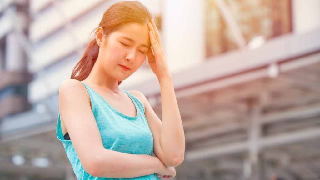Teen girl in athletic wear holding her head in discomfort, illustrating the physical and emotional toll of eating disorders.
