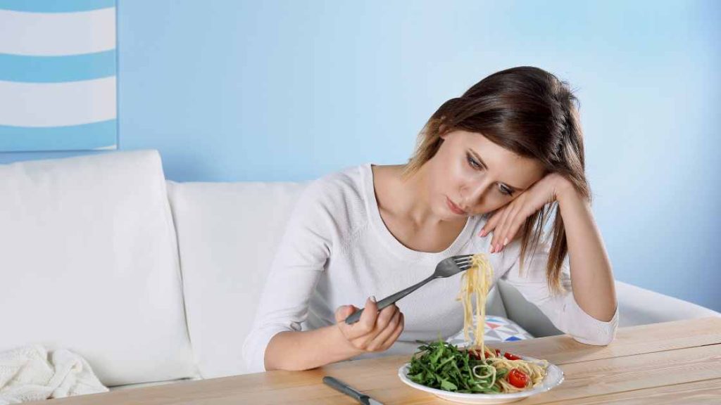 Teen girl with a blank stare twirling pasta on a fork, illustrating emotional detachment and signs of an eating disorder.
