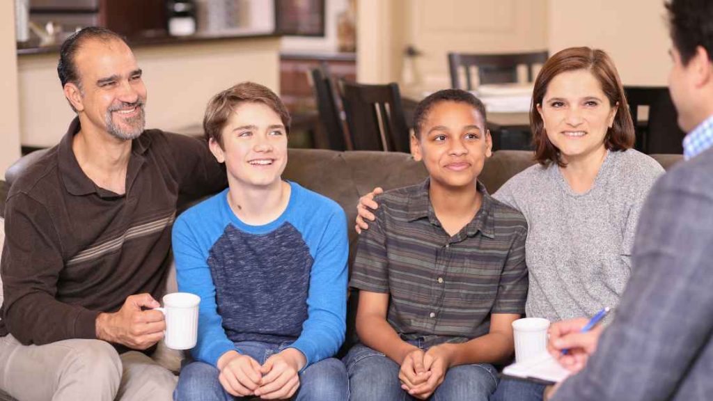 A smiling family sits together on a couch, engaging with a counselor, illustrating the supportive and communicative environment fostered through parent and family counseling.