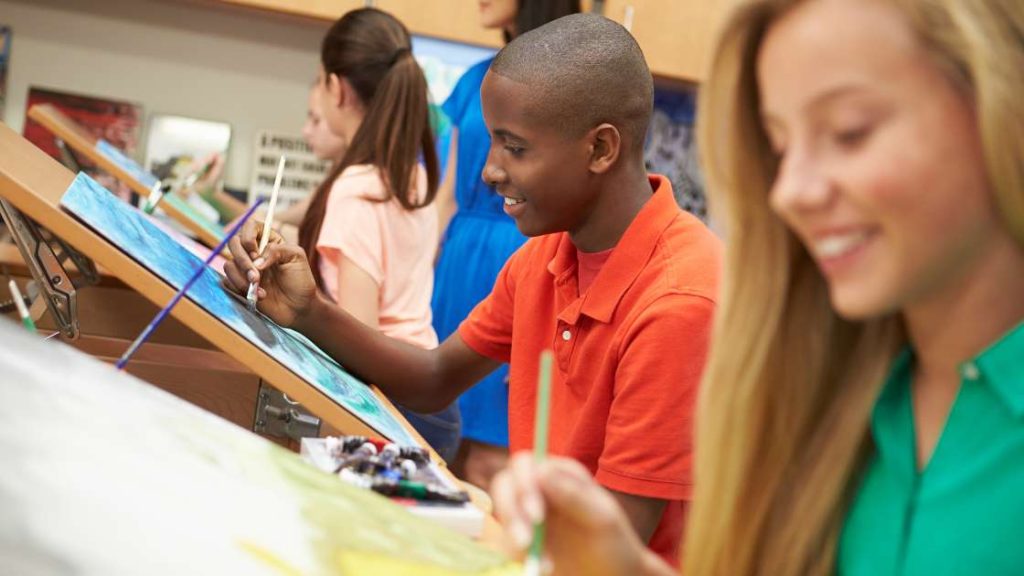 Teenagers happily painting in a classroom setting, illustrating how art therapy encourages creative expression as a therapeutic tool for emotional and mental well-being in teens.