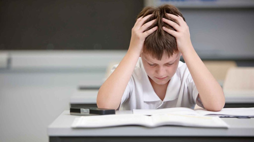 Stressed teen clutching head over textbook and calculator, showing how OCD symptoms affect daily life.