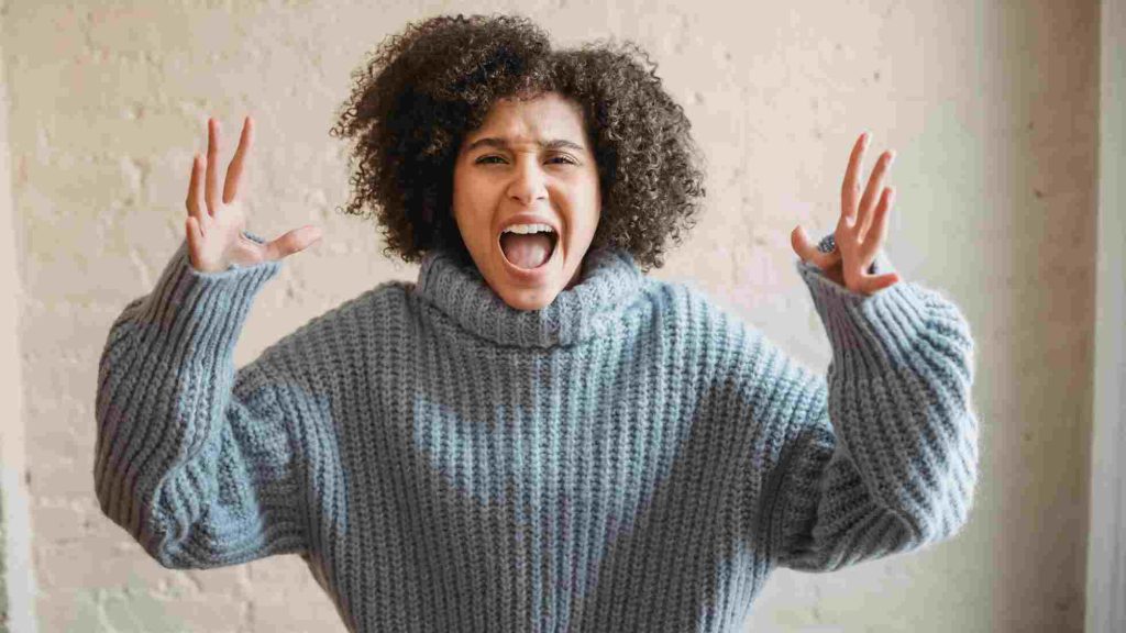 Teen with curly hair screams, hands raised and eyes wide, showing an intense emotional outburst.