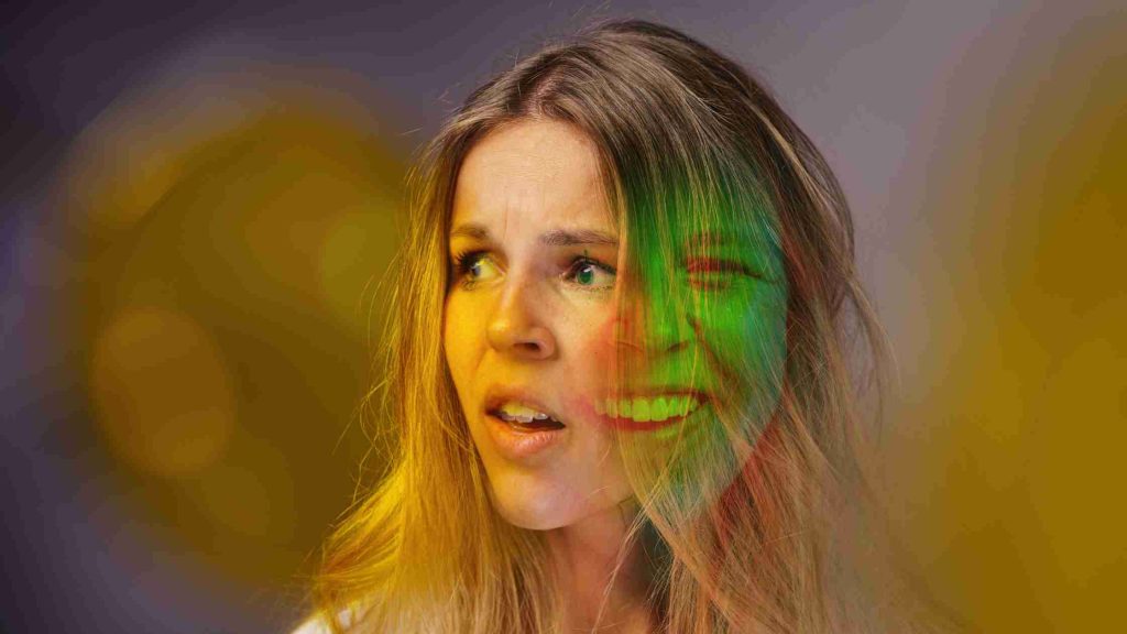 Teen girl’s anxious face overlaid with a faint smiling mask, illustrating sudden mood swings and warning signs of bipolar disorder.