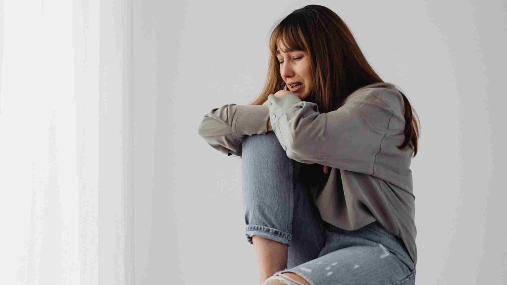 Teen sits curled up, crying into her arms, illustrating the deep emotional toll of chronic stress.