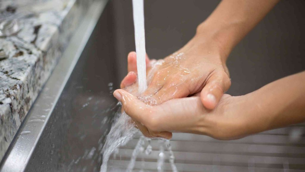 Teen washing hands under running water, illustrating a common behavioral sign of OCD in adolescents.
