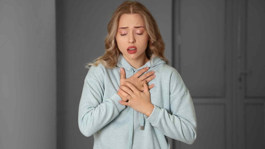 Teen girl holding chest with eyes closed, showing discomfort and distress, representing symptoms of a panic attack.