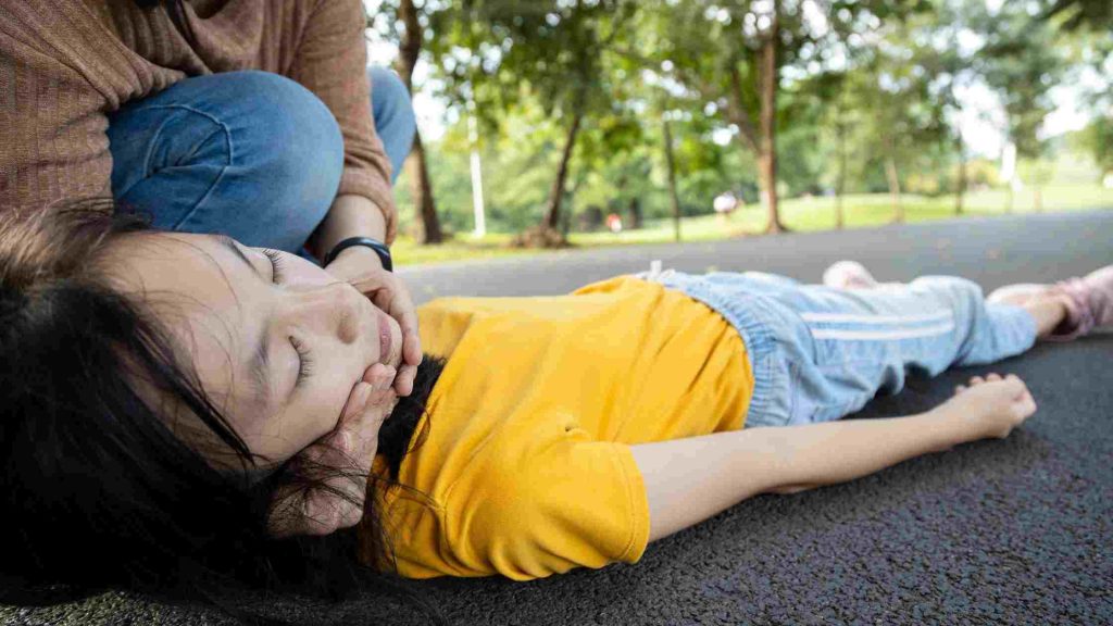 Teen lying on the ground with eyes closed as another person checks her, illustrating response steps during a panic attack.