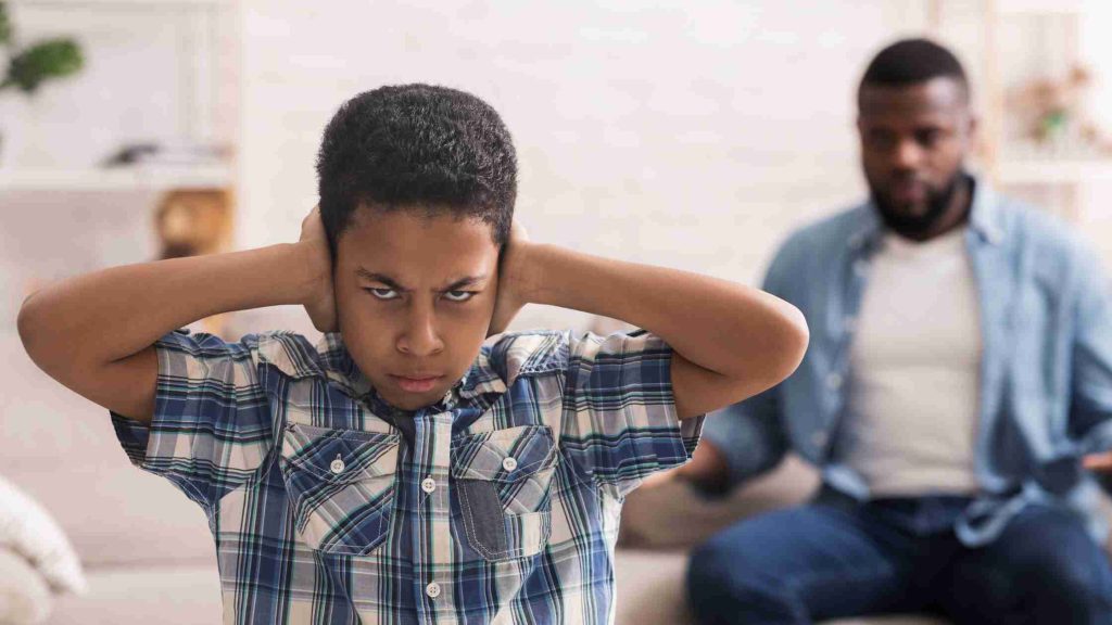 Angry teen covering ears while parent talks, symbolizing conflict and how to respond calmly to a rebellious teen.