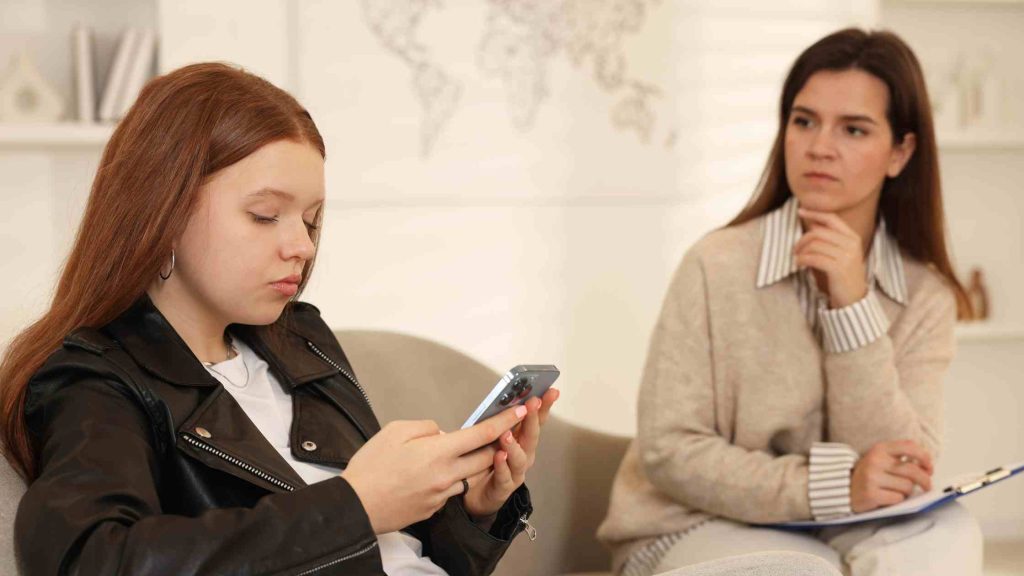 Teen girl ignoring adult while using phone, reflecting the defiant behavior and independence seen in rebellious teens.