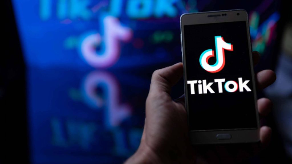 Hand holding a phone with the TikTok logo; the platform’s pull on teen boys and their addictive screen habits.